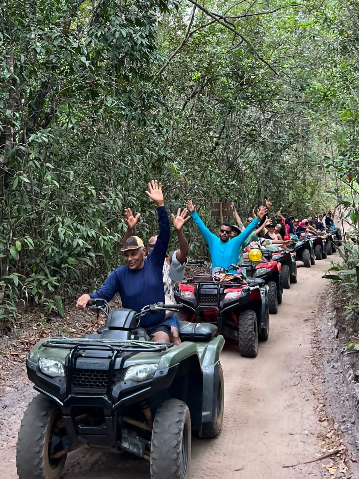 Grupo levantando as mãos nos quadriciclos em meio à vegetação
